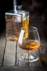 Glass and a bottle of brandy or cognac on the wooden table.