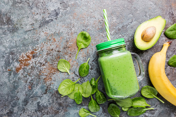 Healthy green smoothie with spinach, avocado, banana and chia seeds in glass jars on gray stone...