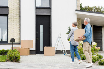 mature man holding box and woman holding plant near new house