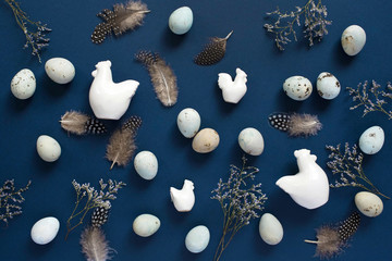 Easter flat lay with eggs, ceramic figurines of chicken and with feathers on blue background. Top view.