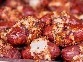 Heap of freshly grilled beef or pork meat sausages covered with spices and sauce at street food festival, selective focus, close-up. Unhealthy oily barbeque street fast food for meat lovers concept