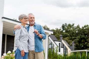 mature man holding keys of new house and hugging smiling woman