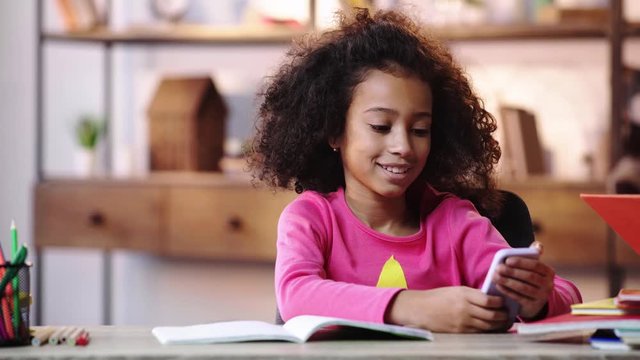 smiling african american child using smartphone while doing homework