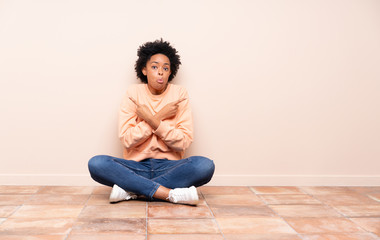 African american woman sitting on the floor pointing to the laterals having doubts