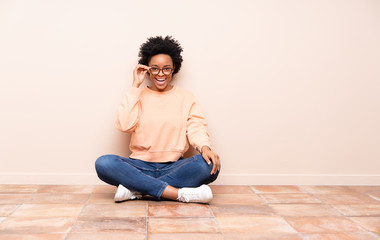 African american woman sitting on the floor with glasses and surprised