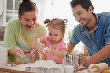 Little daughter preparing cookies with her parents