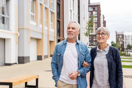 mature man and smiling woman walking near new houses
