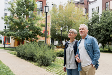 mature man and smiling woman looking away near new buildings