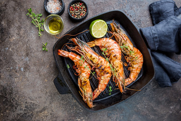 Grilled giant tiger prawns in frying pan with lemon and spices on vintage dark background, top view, copy space. Seafood dinner.