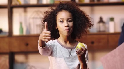 african american child showing thumb up while eating apple - Powered by Adobe