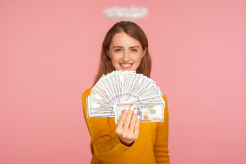 Big income. Portrait of beautiful angelic ginger girl with halo over head holding fan of dollar...
