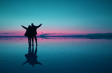 Surreal pop art style silhouette of couple raising arms enjoy the mirror effect of Uyuni Salt Flats, Bolivia, South America