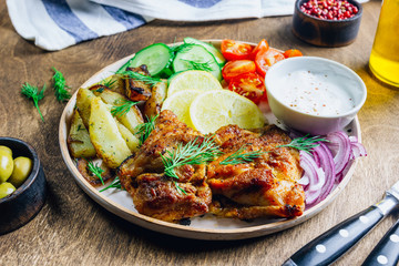 Lunch bowl with grilled chicken, red onion, tomato, cucumber, lemon, olive and sause on wooden background.