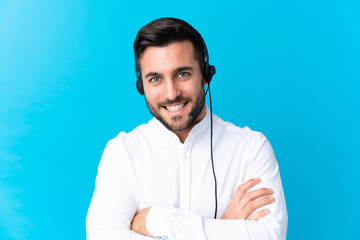 Telemarketer man working with a headset over isolated blue background laughing