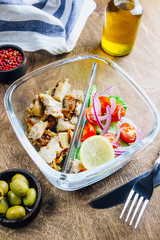 Healthy lunch box with chicken, tomatoes, cucumbers, olive and onion on wooden table. Top view