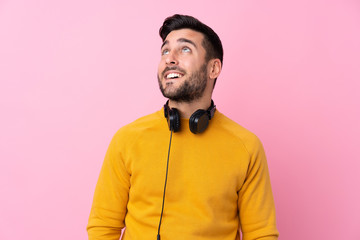 Young handsome man with earphones over isolated pink background looking up while smiling