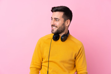 Young handsome man with earphones over isolated pink background looking side
