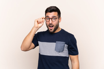 Young handsome man with beard over isolated background with glasses and surprised