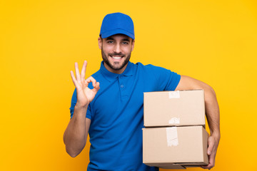 Delivery man over isolated yellow background showing ok sign with fingers