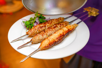 Lula kebab on skewers with red onion and green parsley on a white plate