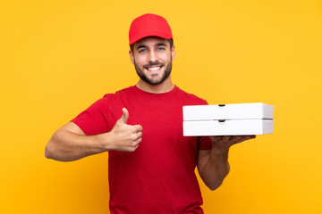 pizza delivery man with work uniform picking up pizza boxes over isolated yellow background with thumbs up because something good has happened