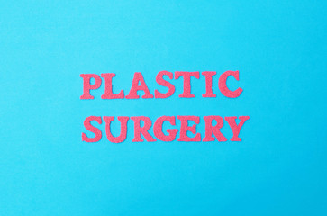 Inscription plastic surgery in red letters on a blue background. The concept of procedures in plastic surgeons abdominoplasty and gynecomastia removal, medicine