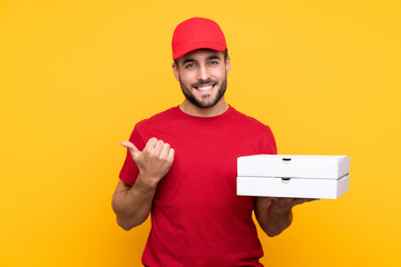 pizza delivery man with work uniform picking up pizza boxes over isolated yellow background...