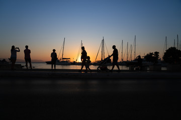 Silhouettes of people admiring the sunrise and yacht masts all back-lit by golden glow
