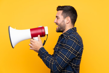 Young handsome man with beard over isolated yellow background shouting through a megaphone