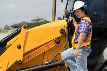 Woman Engineering wearing a white safety helmet standing In front of the backhoe And are using...