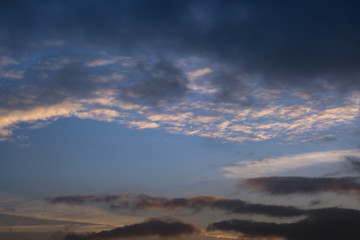 Obraz premium blurred dark sky background with evening fluffy curly rolling clouds with setting sun. Good windy weather