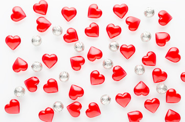 white background with red hearts pattern and silver baubles, flat lay