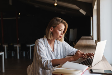 Photo of focused blonde woman typing on laptop while working