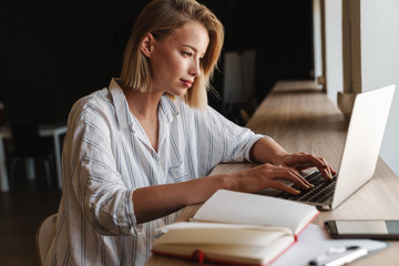 Photo of focused blonde woman typing on laptop while working