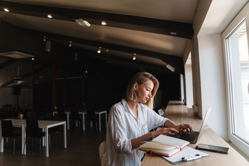 Photo of focused blonde woman typing on laptop while working