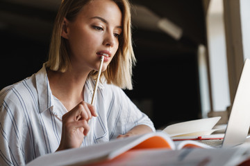 Photo of focused young woman making notes and using laptop