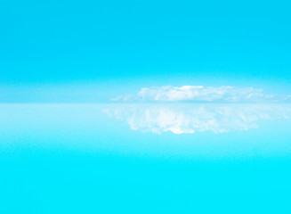 Water and sky, reflection of a large cloud in the water. The cloud is like an iceberg or snowy mountains. Calm background with copy space. Cyan sky and turquoise water.