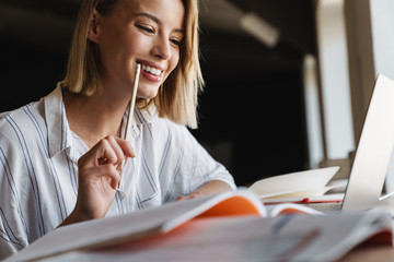 Photo of cheerful young woman making notes and using laptop