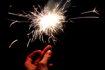 Woman's hand holding burning golden color sparkler in hand in the dark close up on black background view. Soft focus. Copy space. Celebration concept