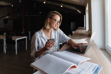 Photo of cheerful caucasian woman using mobile phone and laptop