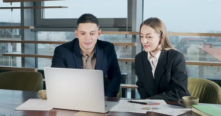 Man and a woman discussing work in the brightly lit modern office. Concerned male and female working with laptop and give five. Business people discuss new startup project concept