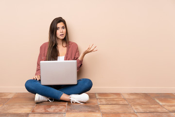 Teenager student girl sitting on the floor with a laptop making doubts gesture