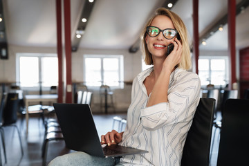 Photo of happy blonde woman talking on cellphone while sitting