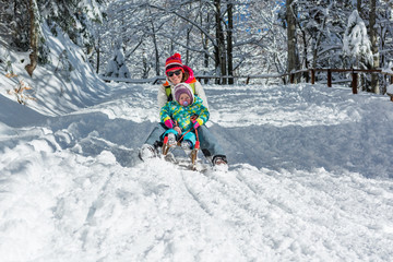 Fototapeta na wymiar Mother and daughter speeding downhill on wooden sledge.