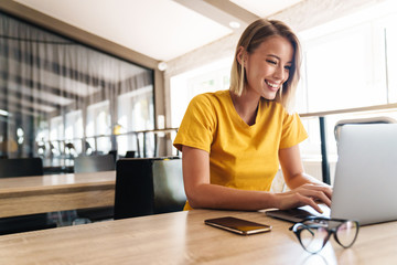 Photo of joyful blonde woman using laptop and smiling