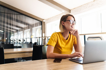 Photo of joyful young woman using laptop and smiling while sitting