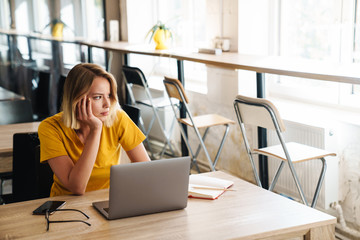 Photo of sad young woman using laptop and looking aside while sitting