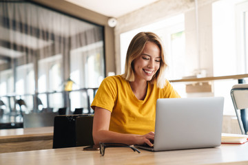 Photo of joyful nice woman using laptop and smiling while sitting - Powered by Adobe