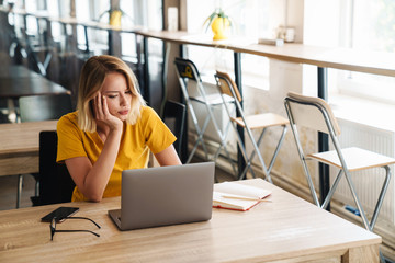 Photo of sad young woman using laptop and looking aside while sitting