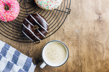 Colorful Donuts breakfast composition with different color styles of doughnuts and fresh coffee on wooden background. Top view. Flat lay
